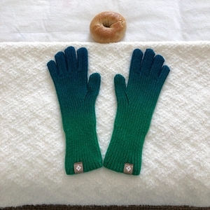 Detail of blue and green gradient knit gloves with logo patch on a textured background