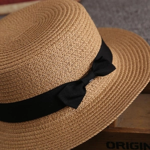Detail of woven straw texture and black ribbon bow on a brown flat top sun hat