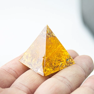 Macro shot of 3cm crystal resin pyramid with gold flakes held in hand palm