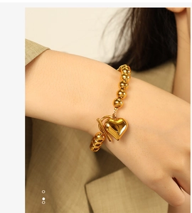 Close-up of golden beaded bracelet with heart pendant and T-bar toggle clasp on wrist