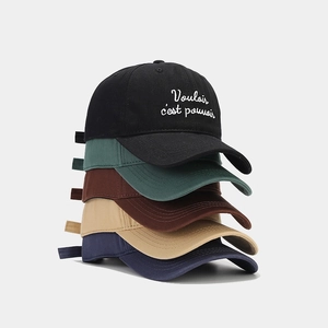 Stack of colorful cotton baseball caps featuring embroidered French quotes on gray background