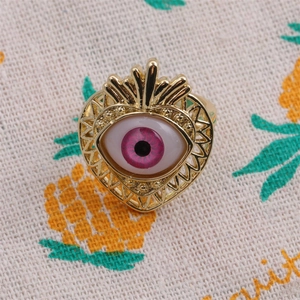 Close-up of gold-plated heart ring with pink zircon evil eye on pineapple burlap background