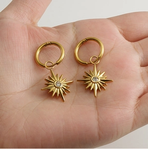 Detail of 18K gold-plated sunflower starburst hoop earrings held in hand for size display