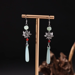 Boucles d'oreilles lotus en argent avec glands verts et perle rouge sur présentoir doré