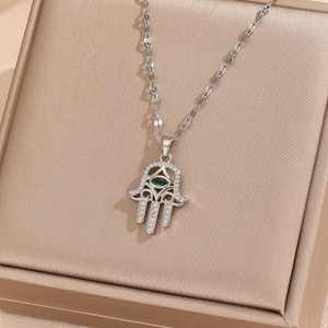 Detailed close-up of Hamsa Hand pendant with green evil eye stone on jewelry box