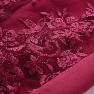 Macro shot of wine red floral lace embroidery on sheer mesh fabric for premium dresses