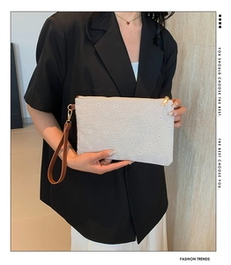 Close-up of canvas clutch bag with floral embroidery and brown leather wristlet strap
