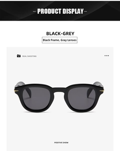 Front view detail of black frame sunglasses with grey lenses and gold arrow hinges