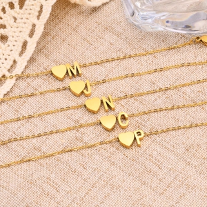 Detailed view of five gold heart bracelets with initials M, J, N, C, and P on beige fabric