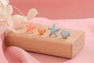 Detailed view of colorful starfish and seashell stud earrings on a textured wooden block