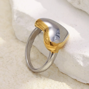 Macro shot of 18K gold and silver heart ring detail on a white textured stone base