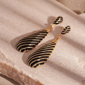 Macro detail of drop earrings with zebra black and gold enamel stripes on marble