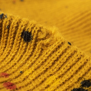Primo piano di un berretto invernale in maglia giallo senape con puntini colorati