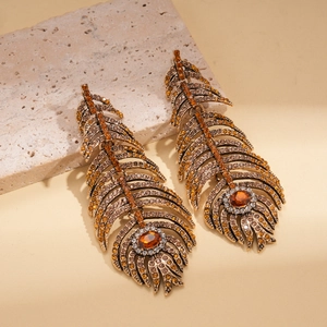Vue détaillée de boucles d'oreilles plume vintage dorées avec pierres ambre sur fond beige