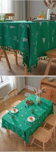 Detail of green Christmas tablecloth featuring white reindeer embroidery and fringe edges