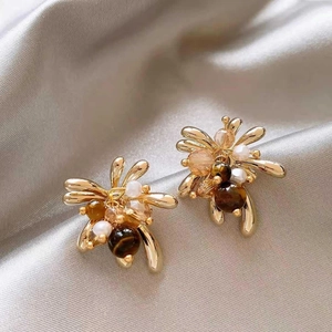 Macro shot of gold floral earrings with tiger eye stone, pearl, and amber crystals