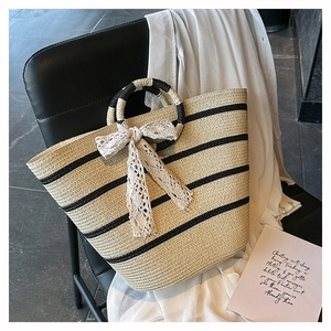 Detail of woven straw tote with black stripes and a large white lace bow accent