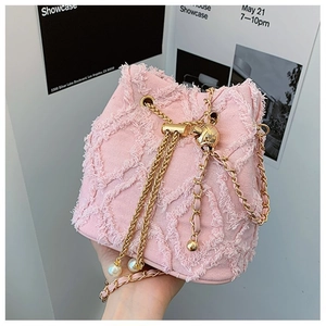 Close-up of pink denim bucket bag with frayed edges, gold chain, and pearl accents