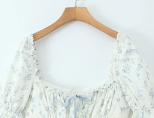 Détail de l'encolure carrée avec volants et imprimé ange bleu sur robe fleurie blanche