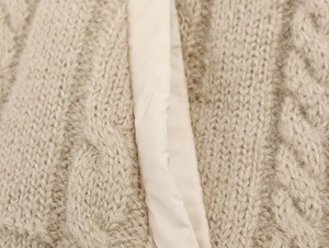 Close-up of beige chunky cable knit vest with detailed textured wool blend fabric