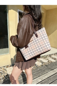 Outdoor shot of a large plaid tote bag with brown leather straps held by a model