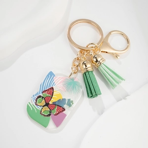 Close-up of a butterfly acrylic keychain with green tassels and gold-tone metal ring