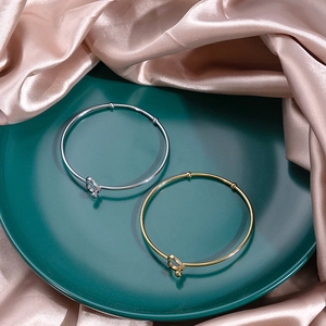 Close-up of gold and silver knotted bangles with heart charms on green ceramic tray