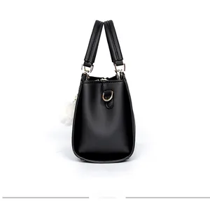 Side view of a black leather handbag with golden hardware and white plush charm accessory