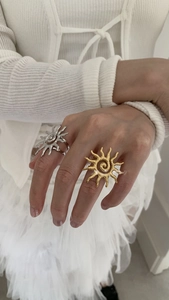 Detail of sun-shaped metallic rings in gold and silver finish worn by a model