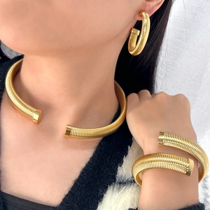 Détail d'un ensemble de bijoux dorés texturés avec collier, bracelet jonc et boucles d'oreilles
