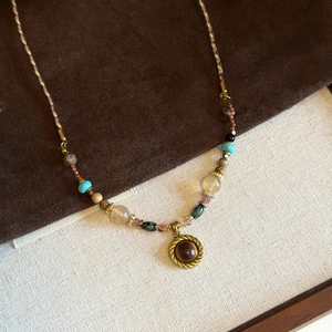 Macro detail of bronze pendant with dark brown tiger eye gemstone on woven beaded chain