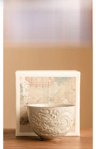 Close-up of a relief dragon motif ceramic teacup with an elegant landscape gift box