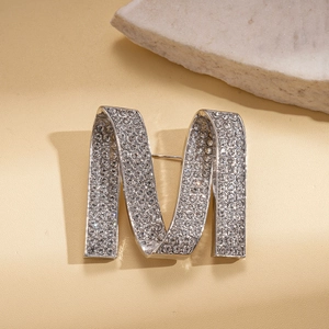 Detailed view of silver letter M brooch with shimmering rhinestones on stone pedestal