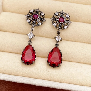 Détail de boucles d'oreilles vintage avec zircon rouge et motif floral dans un écrin en velours