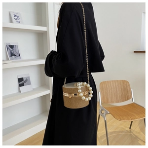 Close-up of woven bucket bag with pearl handle and metal chain on a model