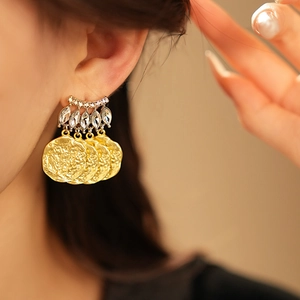 Close-up of vintage gold coin earring with rhinestones worn by a model in soft light