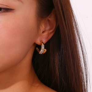 Gros plan de créoles dorées en C avec strass étincelants portées par un mannequin