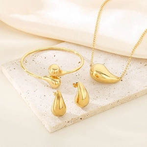 Detailed view of 3-piece gold teardrop jewelry set on stone and silk background