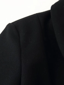 Detailed macro view showing the high-quality wool fabric texture and shoulder stitching of the black coat