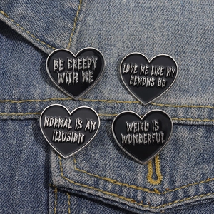 Set of four black gothic heart enamel pins with silver letter slogans on denim background