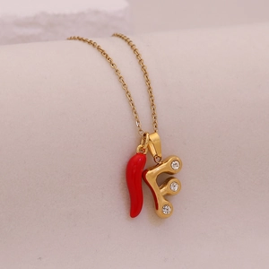 Detail of gold necklace with red chili pendant and sparkling letter F with clear gems
