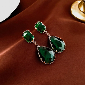 Vintage emerald green drop earrings with gold framing on dark velvet background