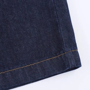 Détail de la texture du denim bleu foncé et des doubles coutures jaunes sur l'ourlet