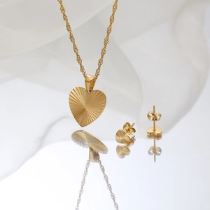 Detailed view of gold heart necklace and earrings with radiant texture on white silk base