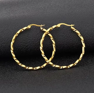 Close-up of golden 18K stainless steel twisted hoop earrings on black leather texture