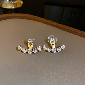 Detailed close-up of golden heart-shaped zircon earrings on a luxury gray display tray