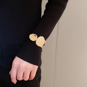 Detail of a minimalist gold double-disc bangle worn over a black knitted sleeve