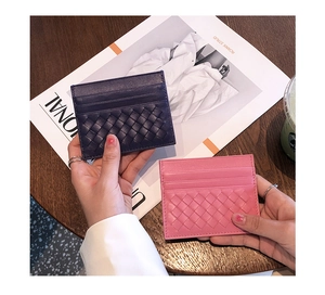 Detail of woven sheepskin card holder in pink and navy blue on a wooden desk