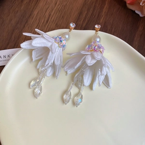 Detail of white chiffon flower earrings with pearls and crystal tassel on ceramic plate