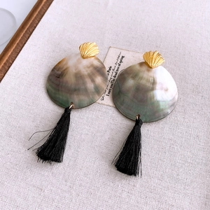 Detail view of shell fringe earrings with golden shell accents on beige linen background